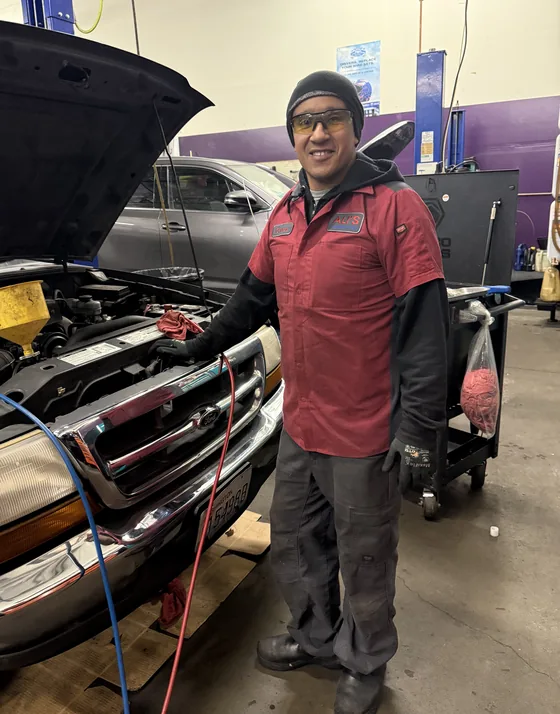 Carlos standing beside a pickup with its hood up in the service bay at Ali's Woodinville Auto Repair