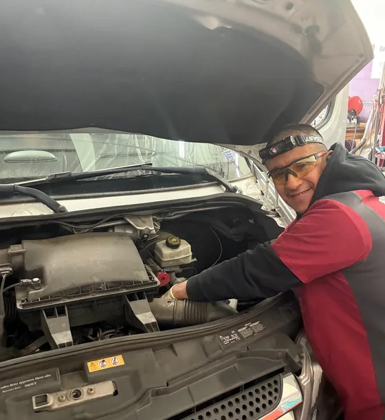 Carlos smiling up from under the hood of a van he is working on