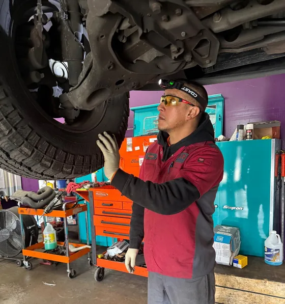 Carlos checking a front wheel and suspension on a truck raised on the lift