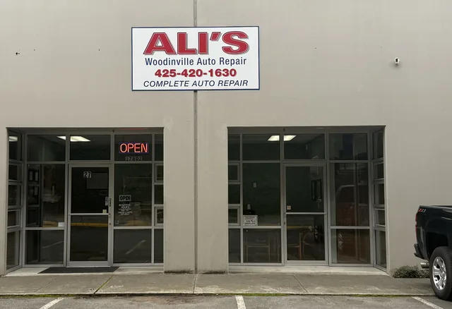 The front door of Ali's Woodinville Auto Repair, suite 27, with the red ALI'S sign above it and the OPEN sign lit