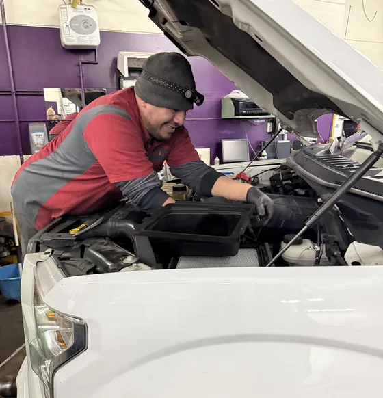 A technician leaning under the hood of a white pickup in the shop